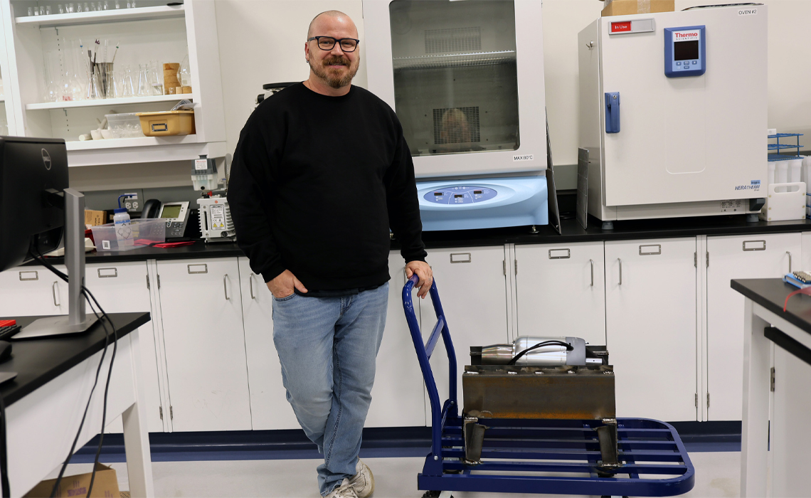 Dr. Kevin Hayes, PhD, stands next to the high-powered engine he will use to research the environmental exposures of those who work on aircrafts. 