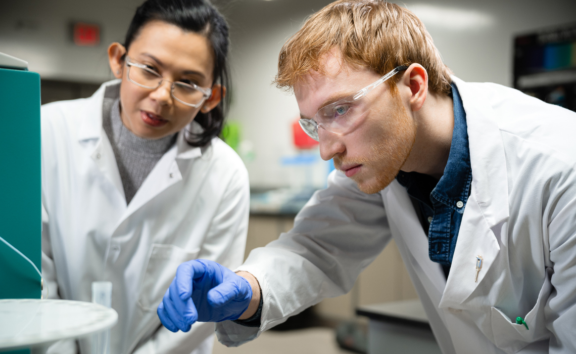 Two individuals in lab coats examining an object together in a laboratory setting.