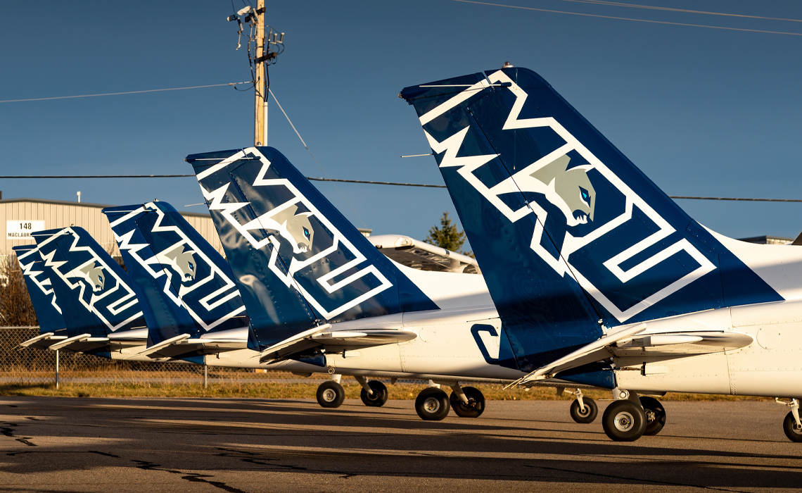 Small planes arranged in a row on a runway, showcasing the Mount Royal University logo.