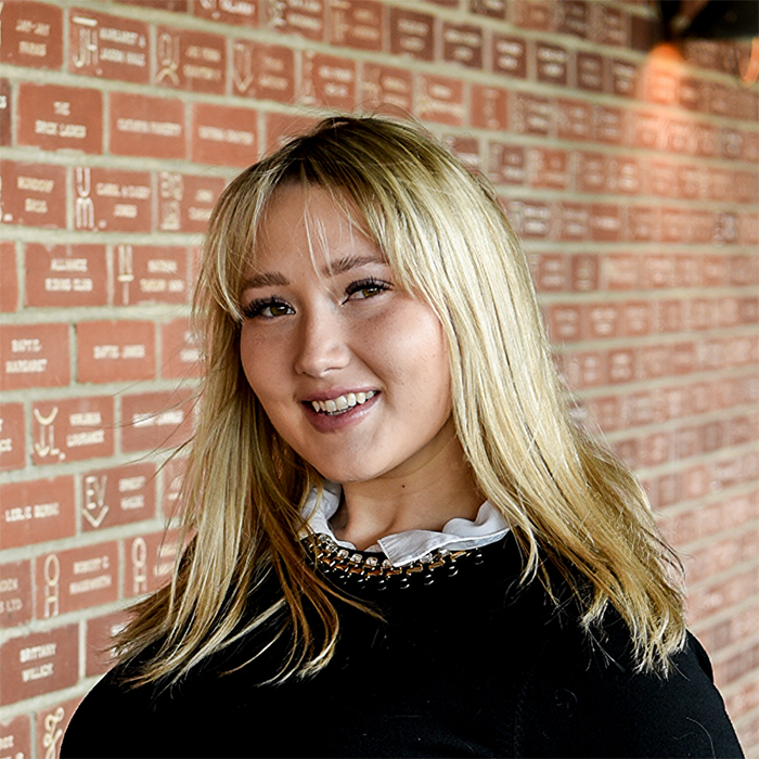 Mikayla Gale stands confidently, dressed in a stylish top against a neutral background.