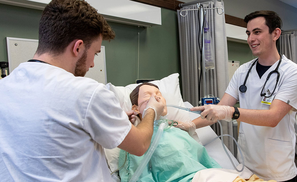Two MRU nursing students practice medical procedures on a training mannequin in the Health Simulation Learning Centre.
