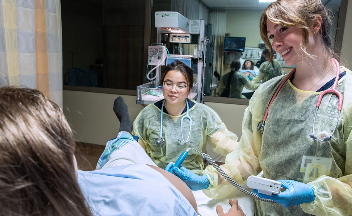 Two Mount Royal University midwifery students administering an ultrasound on a pregnant medical mannequin in the Health Simulation Learning Centre.
