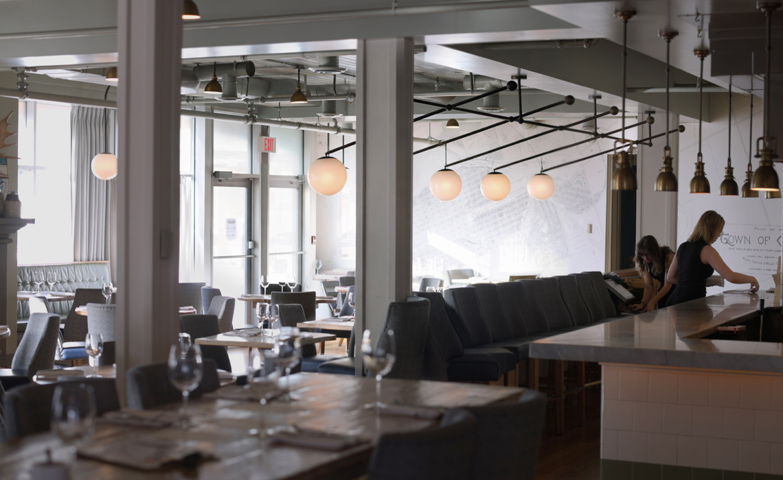 The Nash restaurant interior featuring a long bar and several tables arranged for dining.