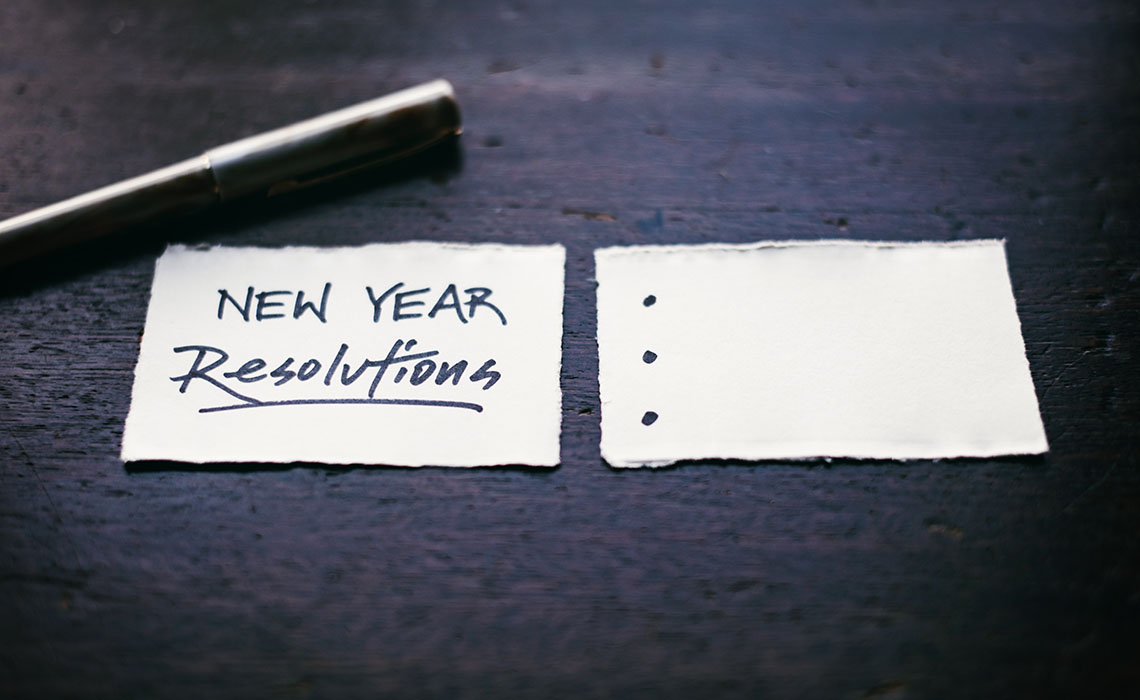 Paper on a desk reading "New Year resolutions" and bullets for a list.
