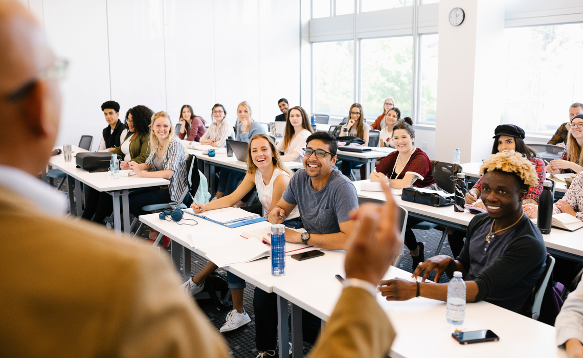 A man lectures to a group of attentive students seated in a classroom setting.