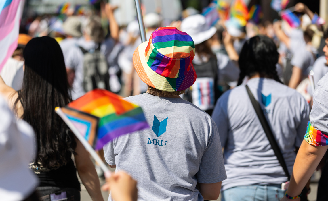 A group of people wearing rainbow hats and shirts marching together down a vibrant city street.