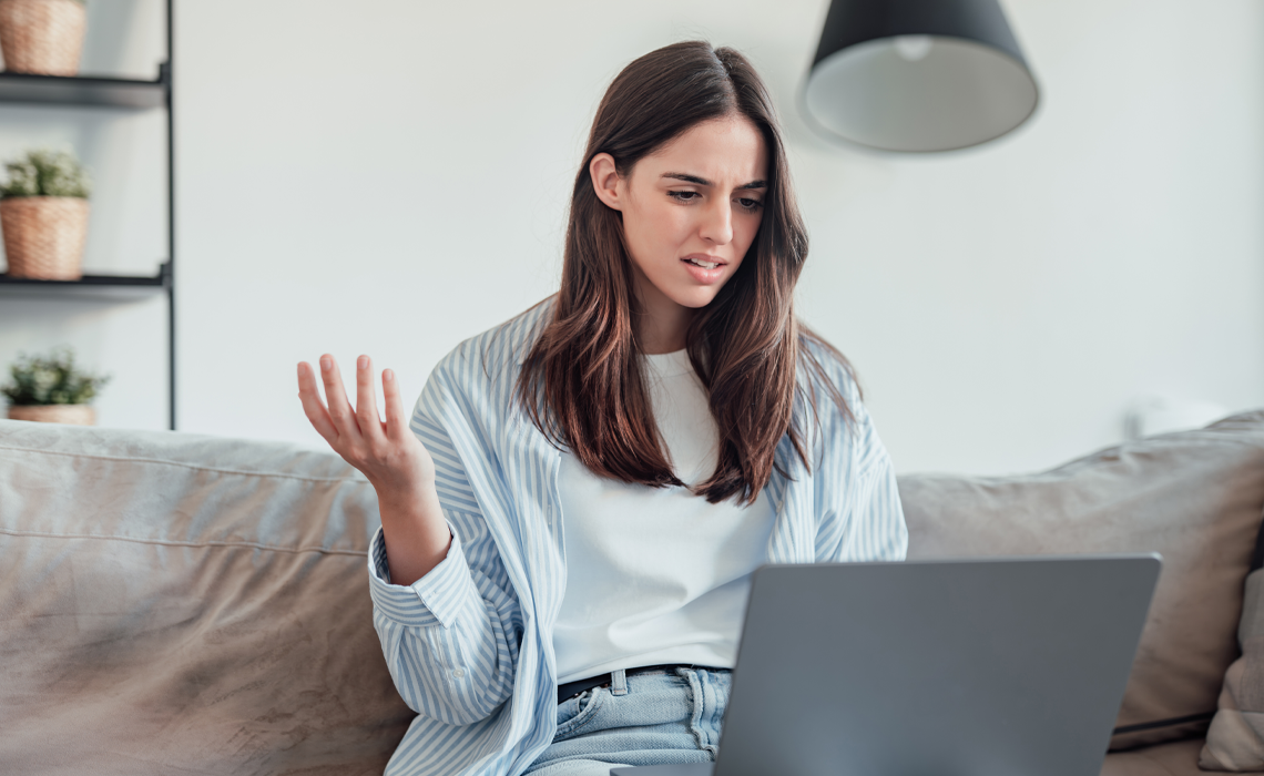 An angry young woman sitting on sofa in living room frustrated; looking at her laptop.