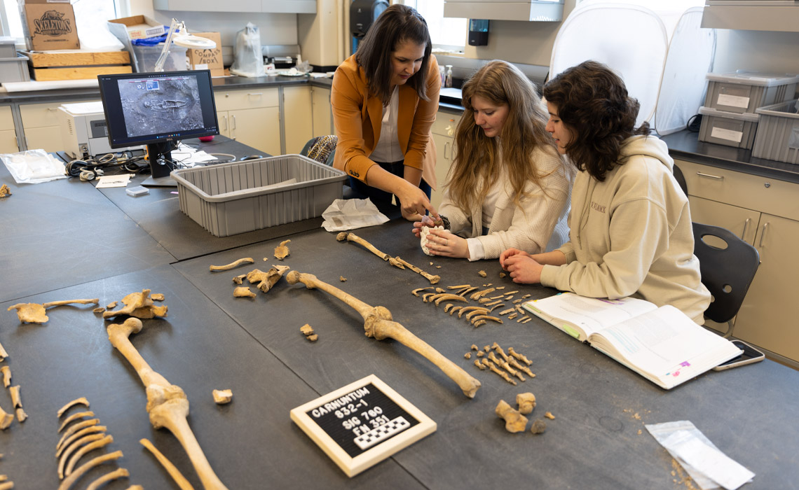 Dr. Rebecca Gilmour, PhD works with alumni assistant Jessica King and and current student assistant Cerena Bond analyzing the remains of an ancient Roman skeleton.