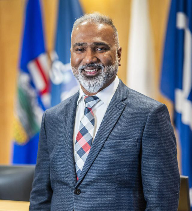 Dr. Ritesh Narayan, PhD, stands confidently in front of multiple flags.