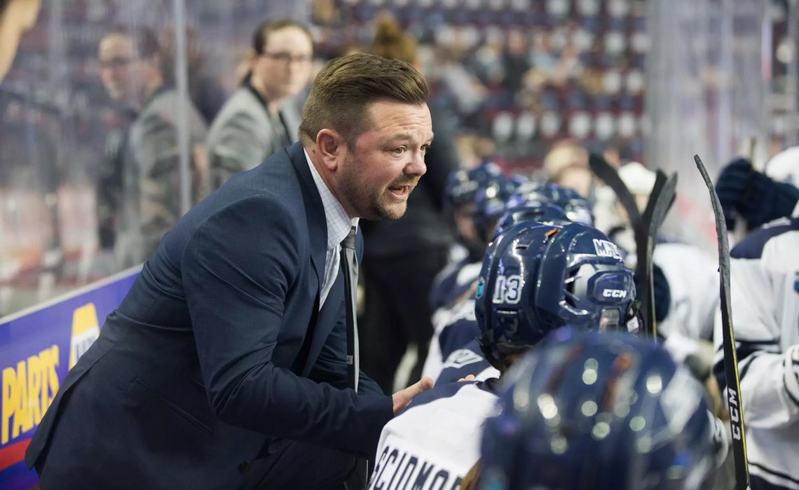 Scott Rivett on the bench speaking with his players during a game.