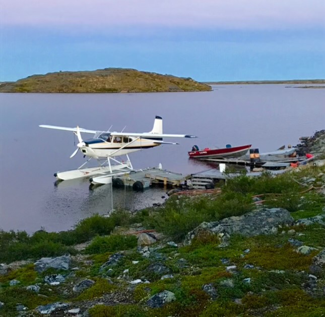 A small plane parked on the shore of a tranquil lake, surrounded by greenery and reflecting the sky.