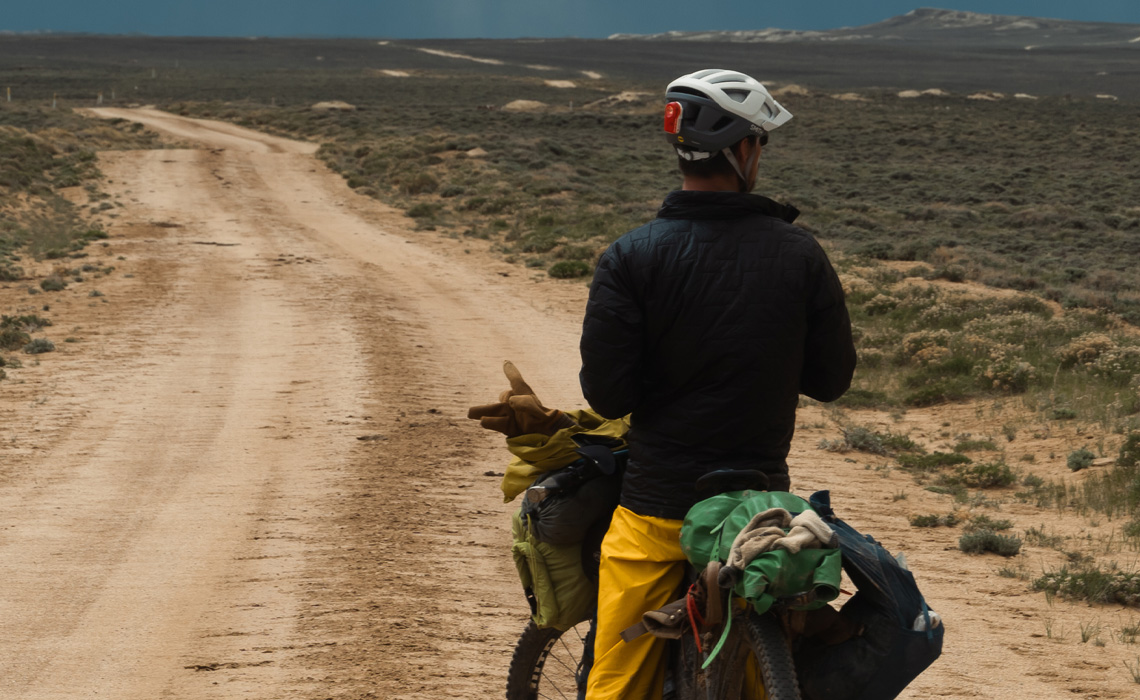A man riding a bike on a dirt road, surrounded by nature's beauty.