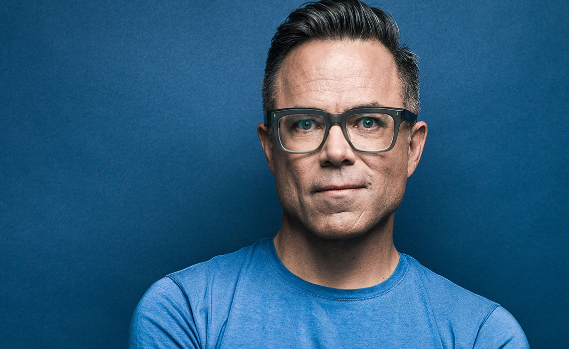 Timothy Caulfield wearing glasses and a blue shirt, looking directly at the camera with a neutral expression.