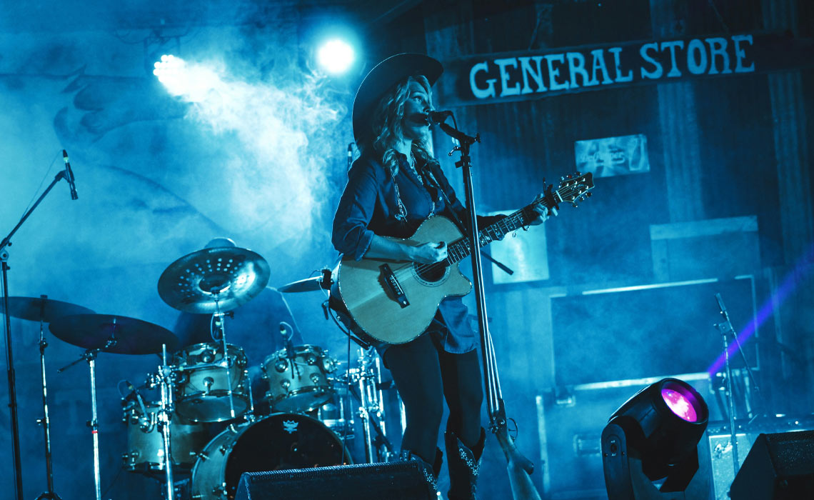 A musician in a cowboy hat performing with a guitar on stage.