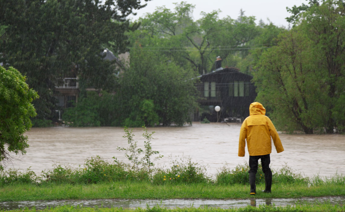 A person wearing a yellow raincoat observes a flooded property.