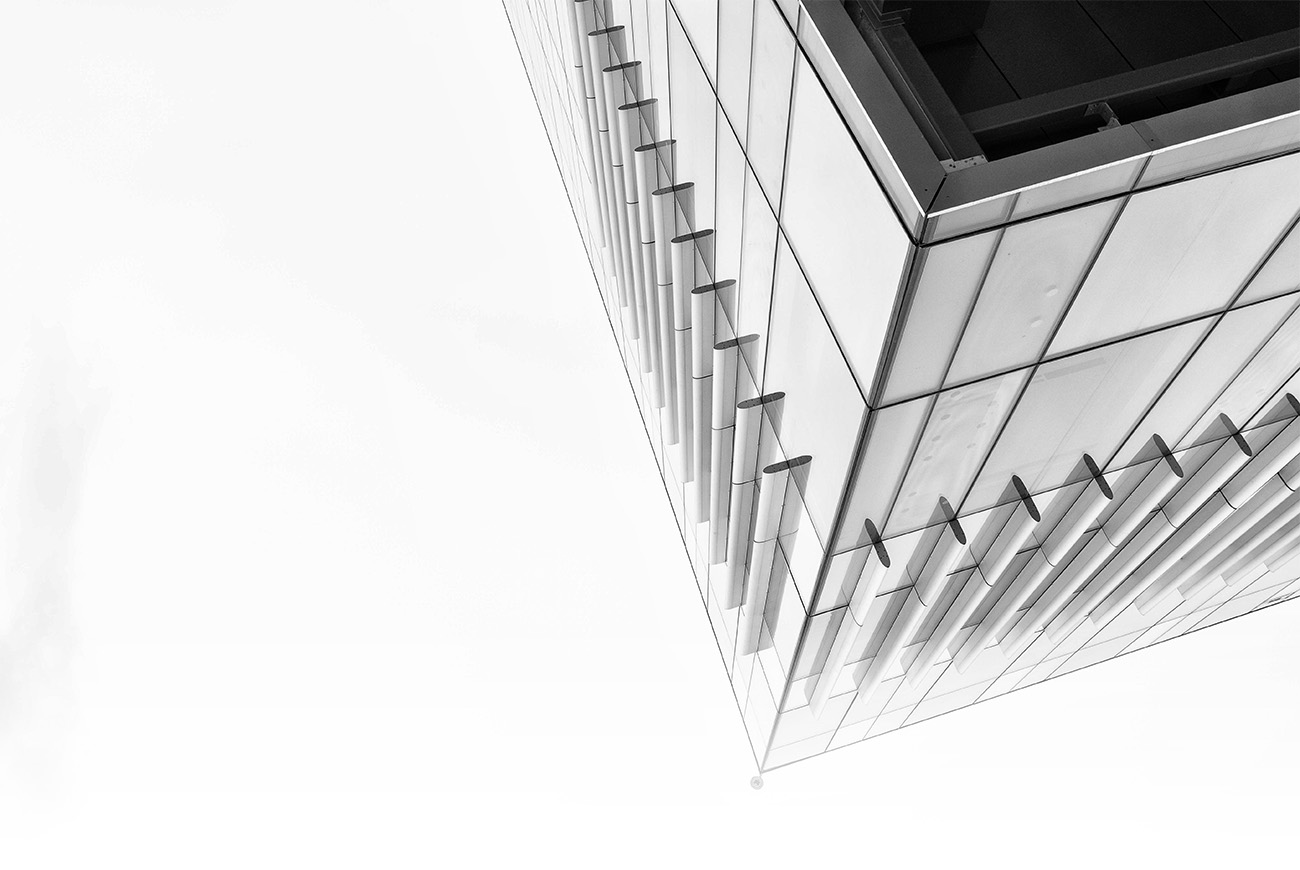 Black and white photo of the side of the Riddell Library and Learning Centre from below. A glass windowed building with metal ridges looking up at a clear sky.