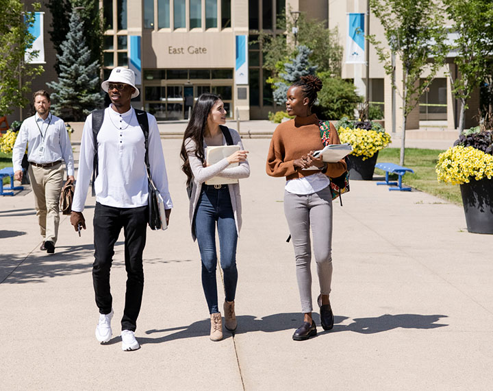 Three students walking away from East Gate and chatting on a nice summer day.