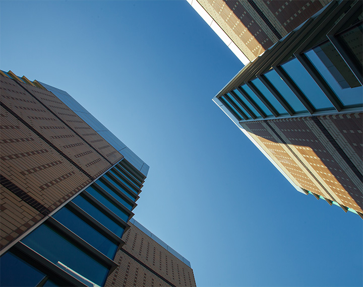 Photo of West Residence looking up into a blue sky. The corners of the image have two brick and glass windowed buildings.