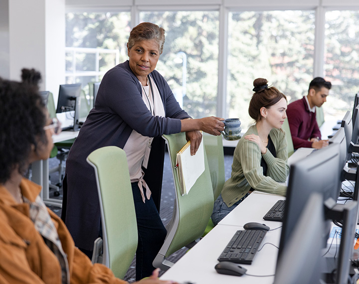 A professor chats with students working on projects in a computer lab.