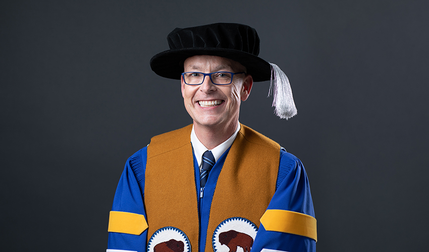 Tim Rahilly, PhD, is pictured wearing the robes of the presidential office, which have four chevrons on the sleeves instead of the usual three. Rahilly's robe is also adorned with the colours of the Indigenous medicine wheel, which represent each of the four directions (east, south, north and west) at the bottom of the sleeves and the hem. The robe is topped with a leather stole designed by Moonstone Creation featuring two beaded buffalos facing each other.