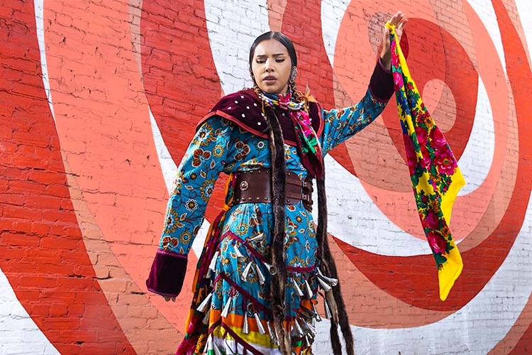 Sofia Eaglehead Baptise in a jingle dress dancing in front a mural in downtown Calgary.