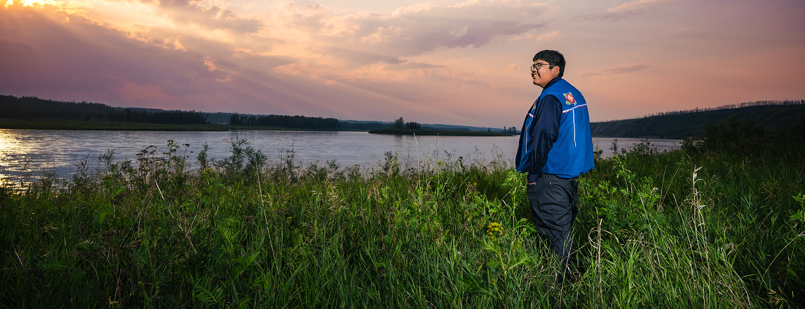 Samuel Metacat-Yah looking out over a river and fiery sunset.