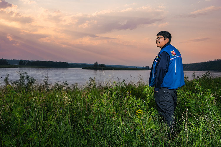 Samuel Metacat-Yah looking out over a river and fiery sunset.