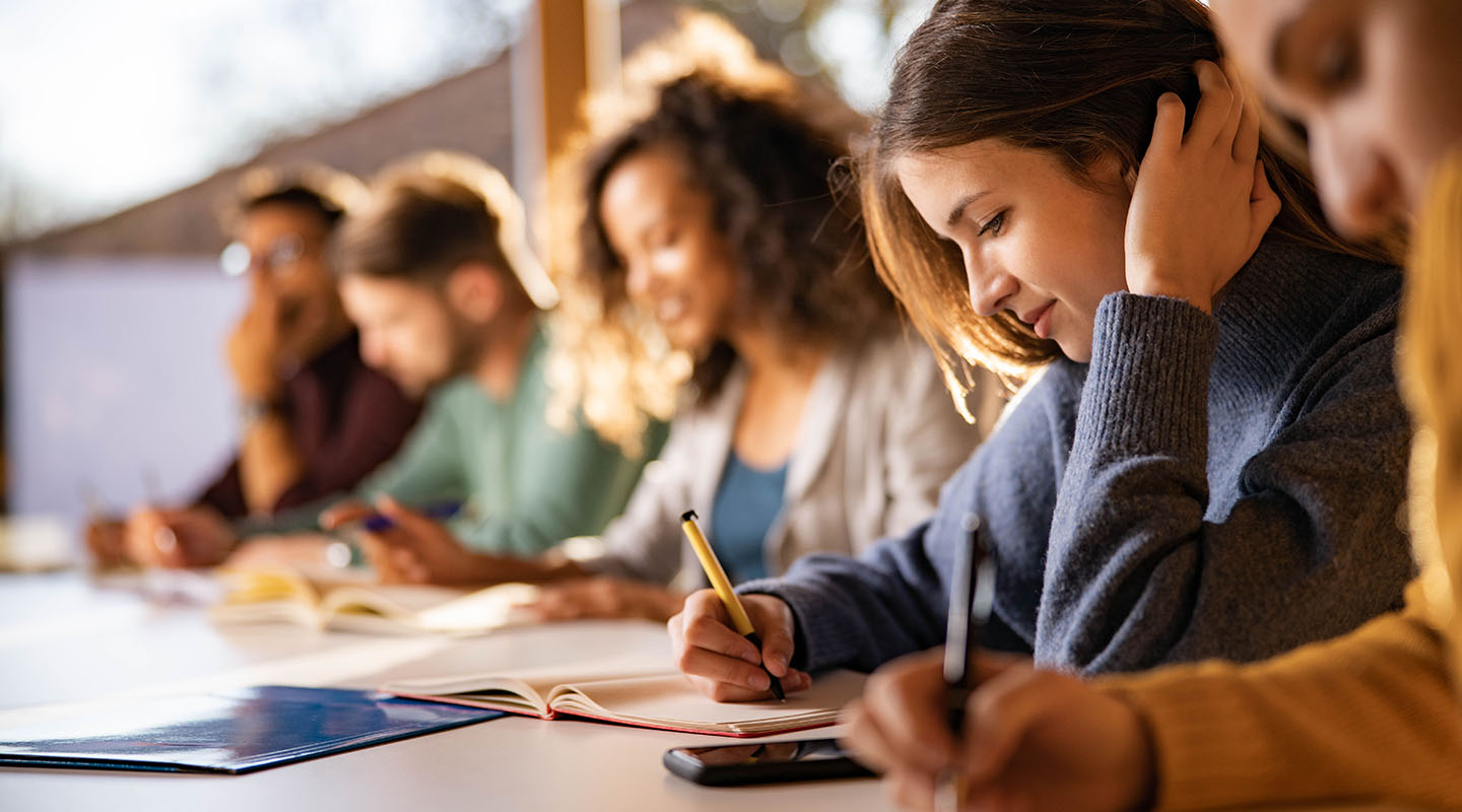 A long desk with several students taking notes.