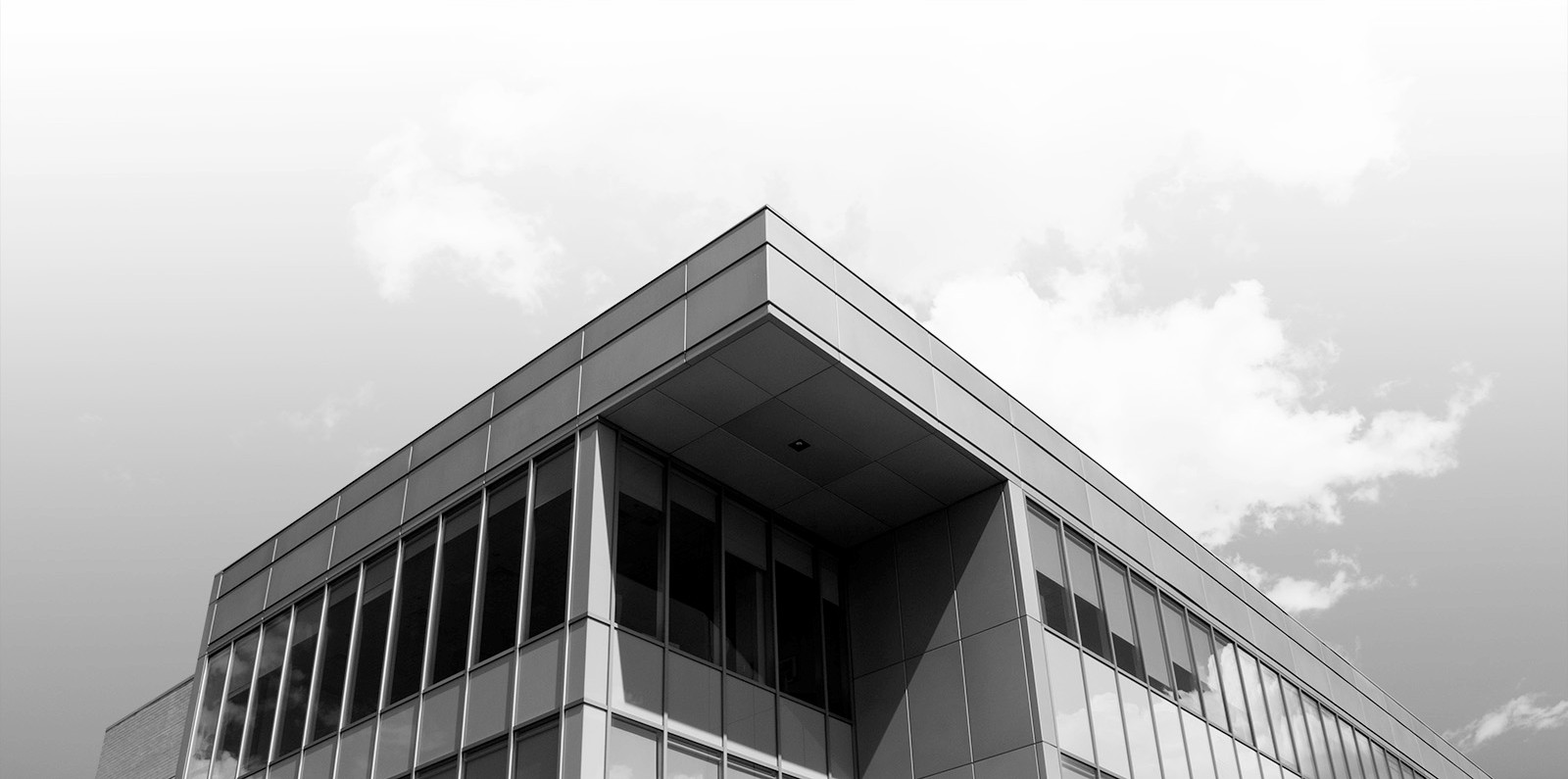 Black and white photo looking up at the corner of of the Bissett School of Business - a glass and metal rectangular building.