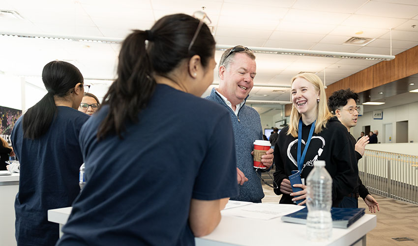 Two Open House attendees chatting with an MRU representative in the Bissett School of Business.