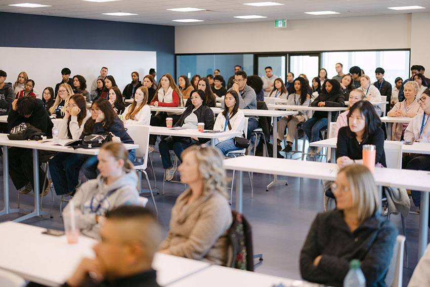 Rows of students at desks during a live panel presentation.