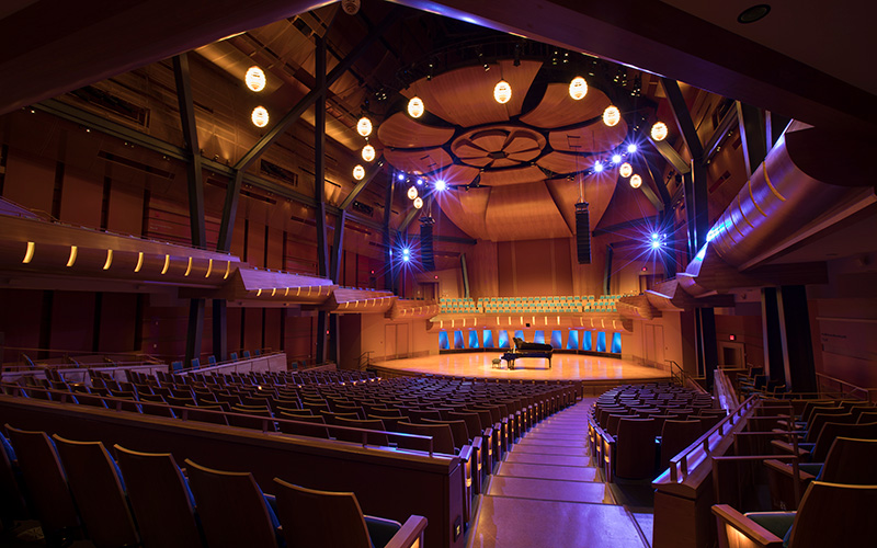 A concert hall made of warm wood, dramatically lit with blue lights.
