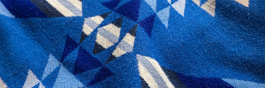 Close up of a blue blanket with geometic shapes in whites, blues and blacks.
