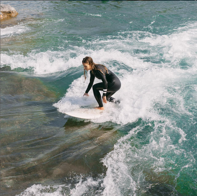 A surfer riding the waves wearing a Honubelle Swimwear wet suit.
