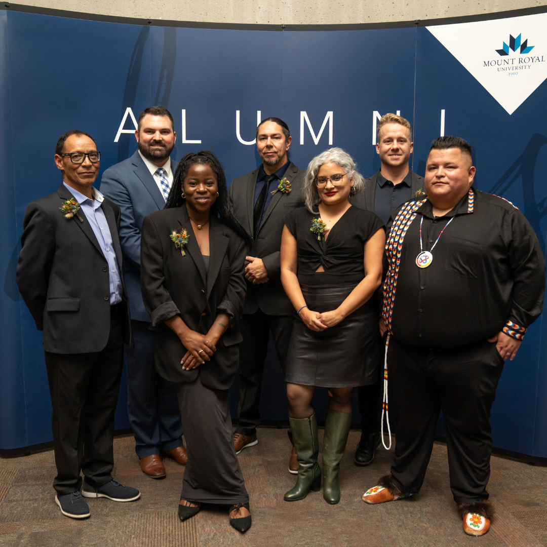 Winners of the Outstanding Alumni Awards posing in front of an Alumni banner