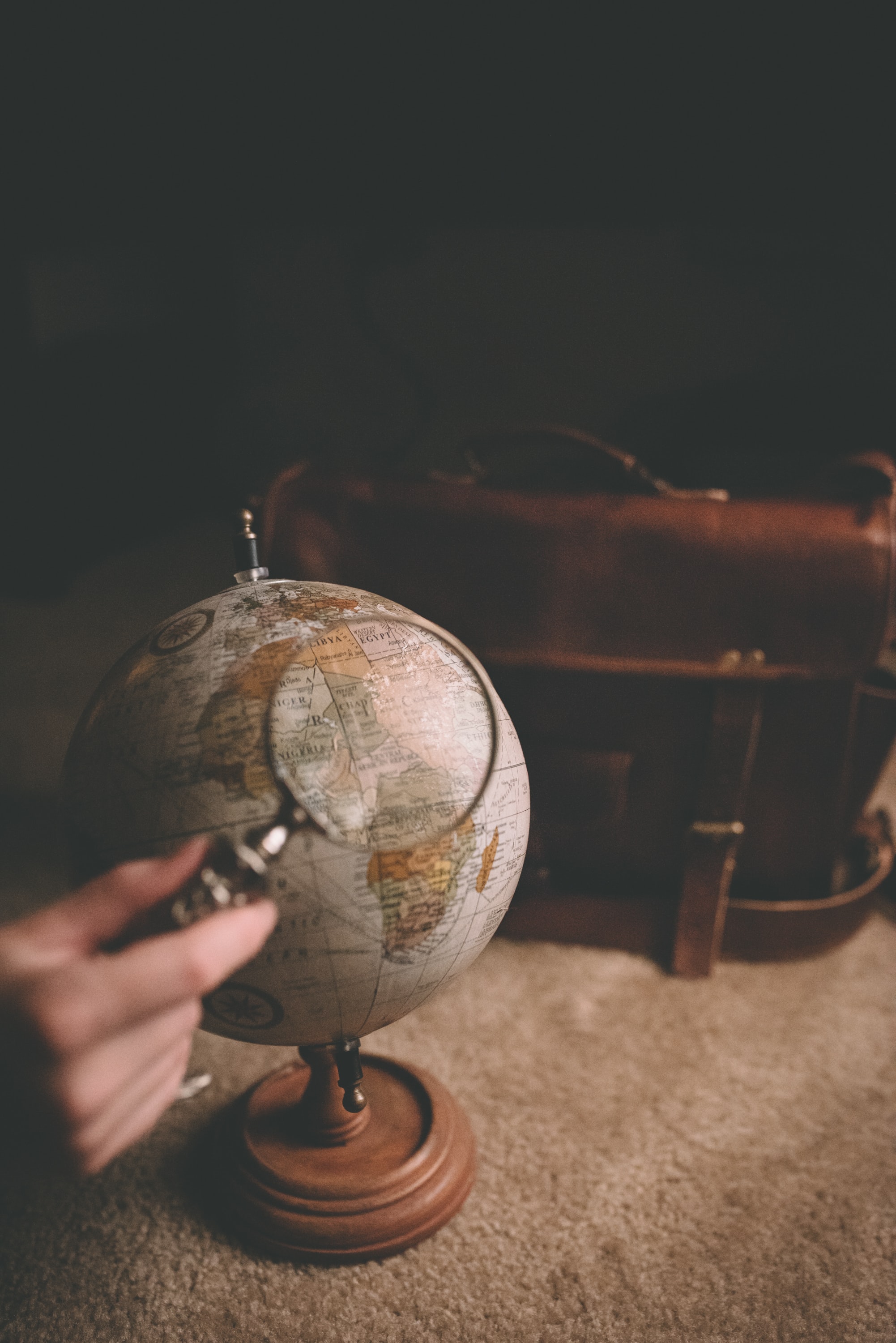 Hand holding a magnifying glass up to a globe.
