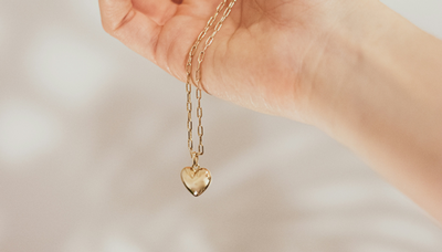 A hand holding a gold locket on a gold chain.