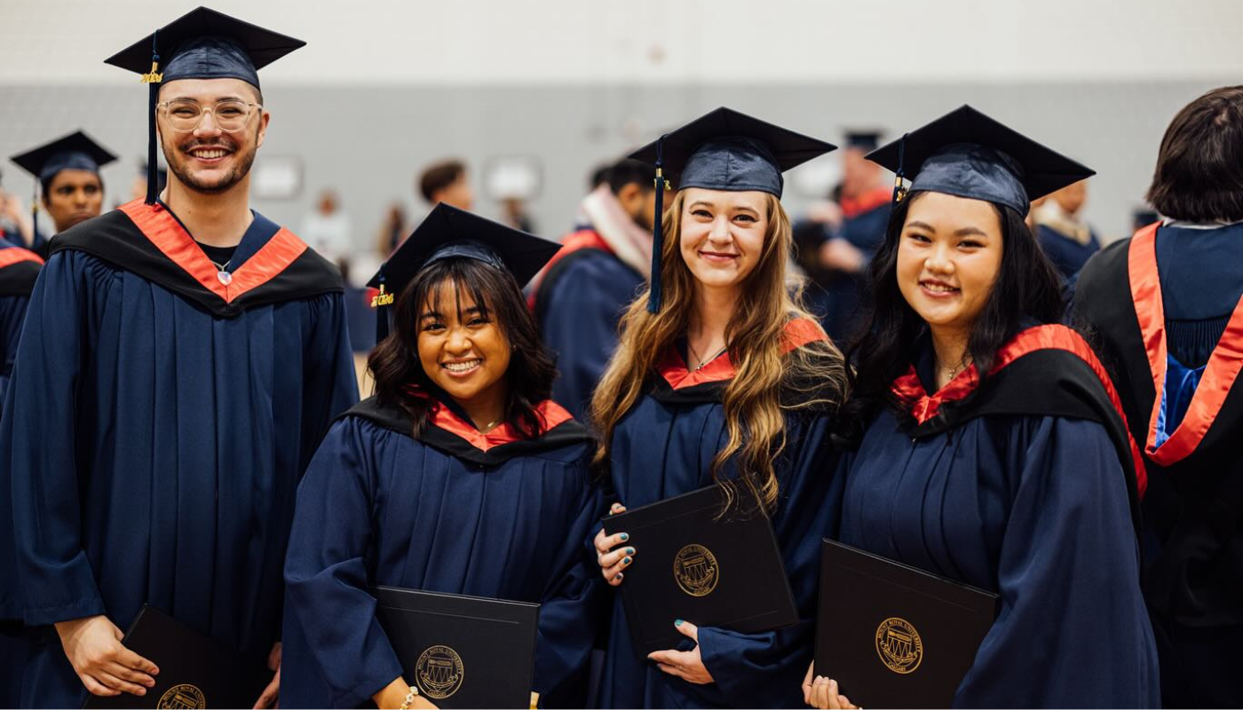Four communications graduates in their caps and gowns posing for a photo