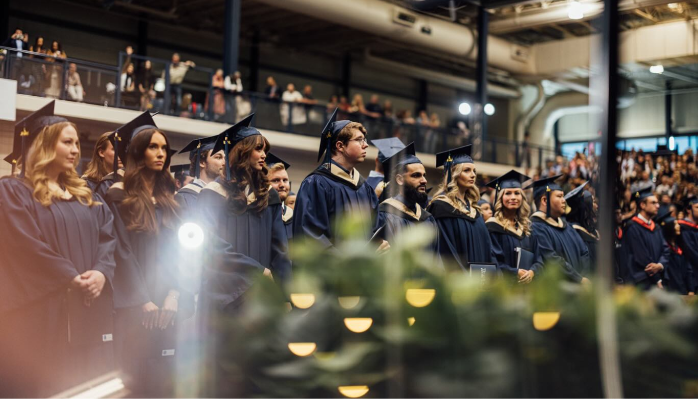 Rows of graduating students in the Triple Gym standing for a part of Convocation.
