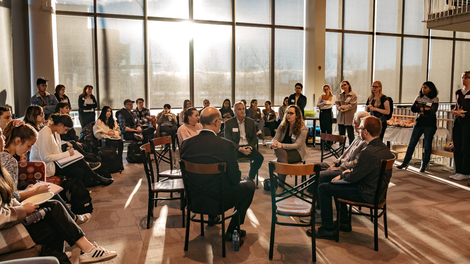 Group of professionals having a roundtable discussion with many people watching and taking notes.