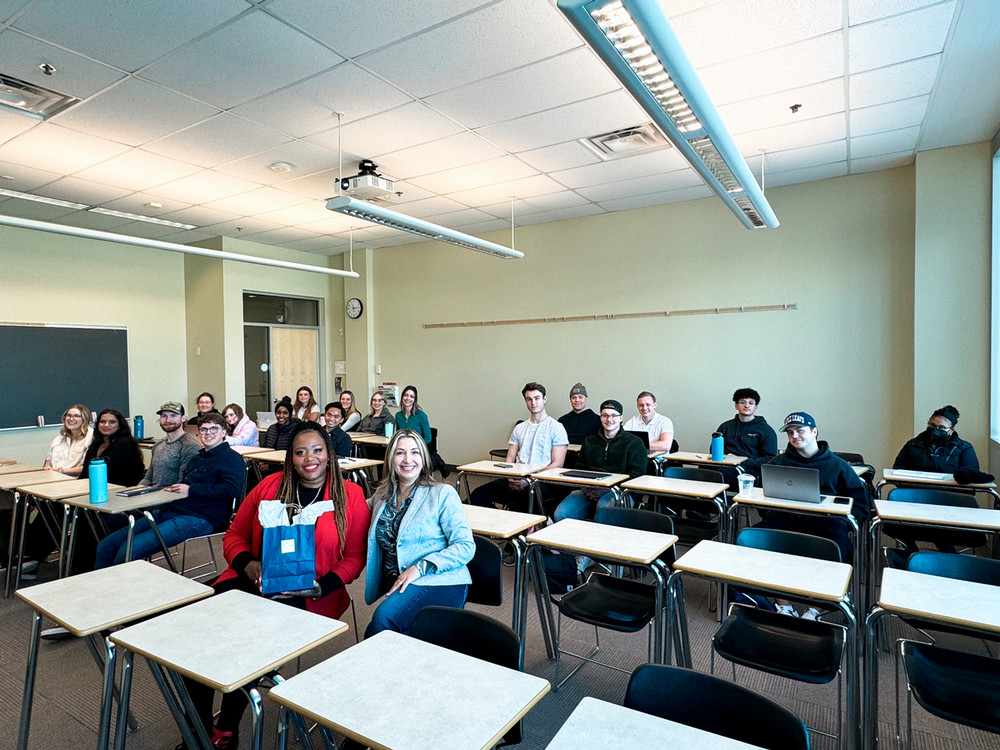 A classroom of students and an alumni speaker posing for a photo.