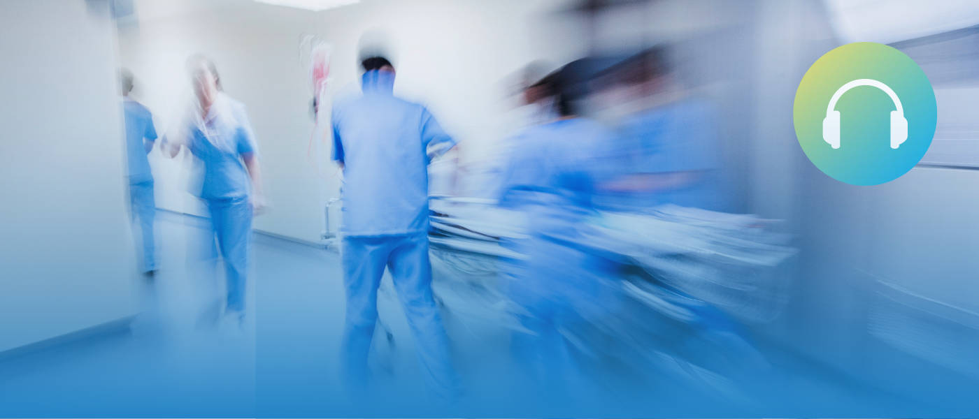 People in scrubs wheeling a gurney down a hallway with a motion blur effect.