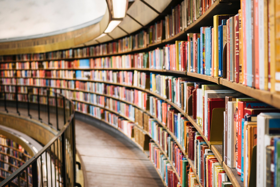 A curved wall of bookshelves filled floor to ceiling with books and a railing over more bookshelves below.