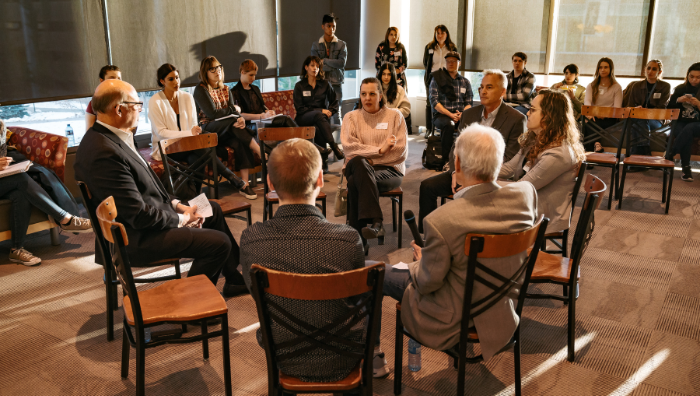 A group of people sitting in a circle having a discussion while people outside the circle spectate.