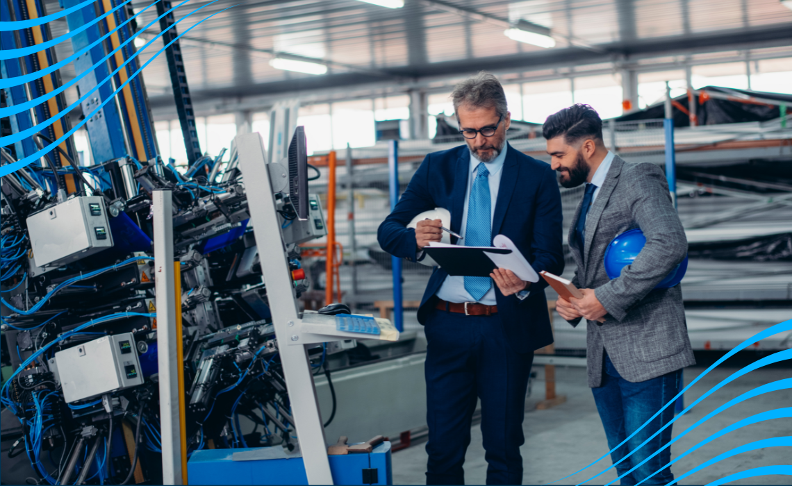 Two men read from a clipboard while standing in a manufacturing facility