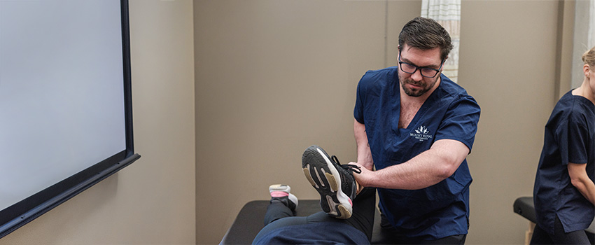 A massage therapy student stretching a clothes client on a massage table.