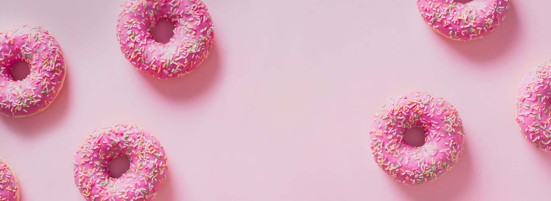 A pattern of pink, spinkle-covered doughnuts on a light pink background.