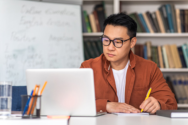 A man takes notes while he listens to an instructor laptop.