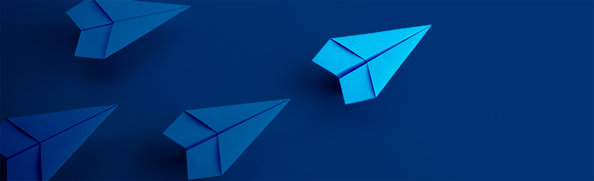 A fleet of paper airplanes is led by a slightly different coloured airplane.
