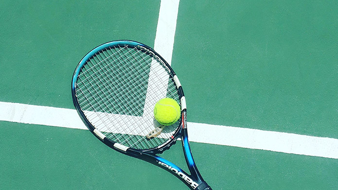 A tennis racquet and ball on the ground of a tennis court.